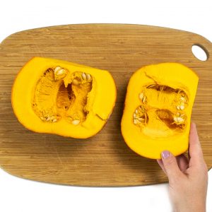 Pumpkin on a cutting board chopped in half.