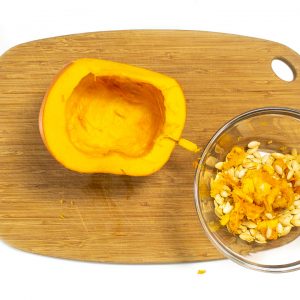 Pumpkin on a cutting board with seeds out and in a bowl.