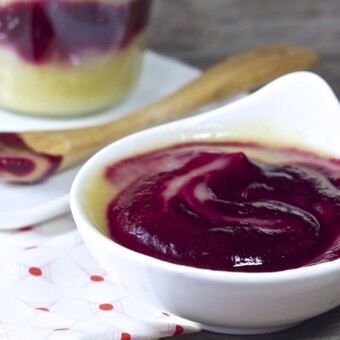 Small white bowl filled with homemade beet and apple baby food puree with a jar behind it.