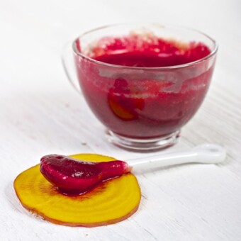 clear jar filled with red beet puree with a spoon sitting in front of it resting on a piece of golden beet.
