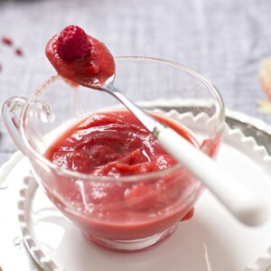 Image of raspberry and apple puree in a glass bowl with a spoon resting on top.