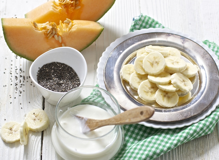 Spread of produce - bananas, cantaloupe and chia seeds on a white background.