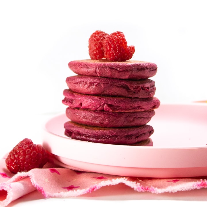 Stack of pink pancakes with raspberries on top.