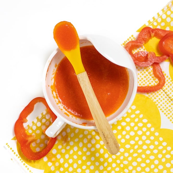 White bowl filled red pepper puree with yellow spoon.