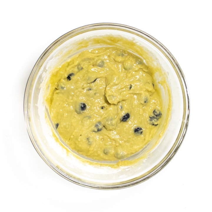 Clear glass bowl of blueberry avocado muffin batter.