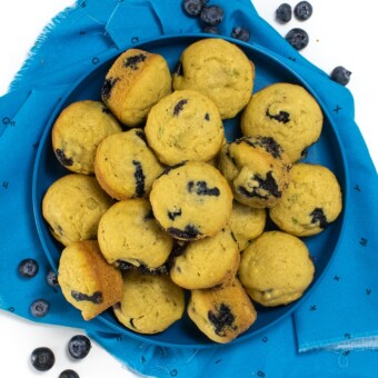 Blue kids plate with blueberry muffins pilled high and blueberries scattered around.