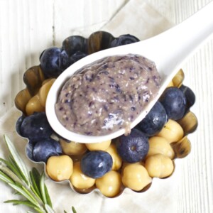 Spoon filled with baby food puree rising on a dish filled with blueberries and chickpeas.