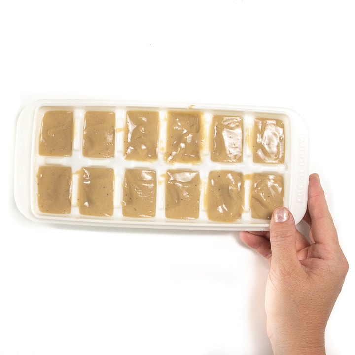 A hand holding a freezer tray full of a banana puree for baby.