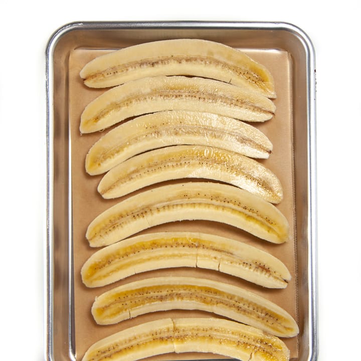 bananas lined up on a baking sheet ready to get roasted for a baby food puree.