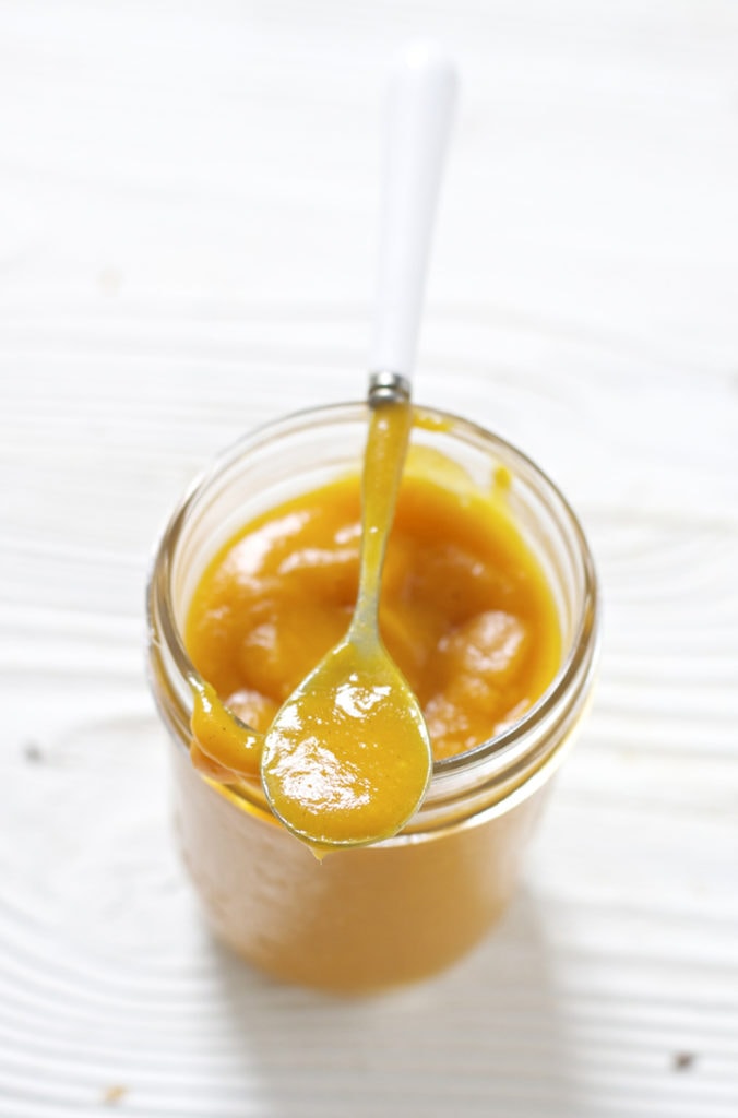 Glass jar filled with a thick homemade baby food puree with a spoon resting on top.