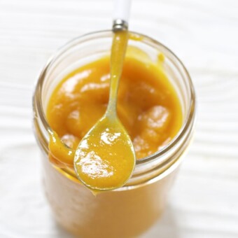 Glass jar filled with a thick homemade baby food puree with a spoon resting on top.