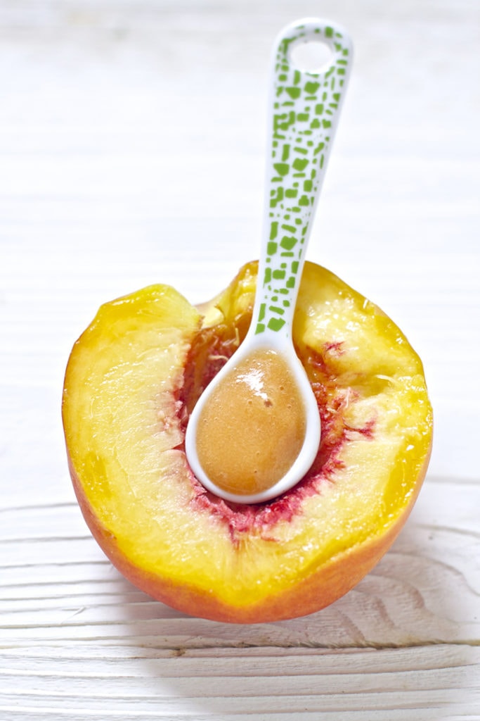 half a peach with a spoon full of baby food puree inside.