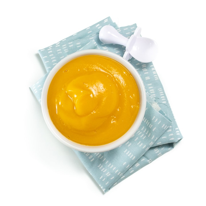 Small bowl of butternut squash puree along with a blue napkin and white baby spoon.