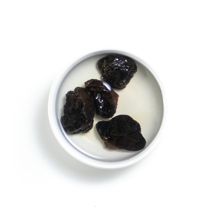 Small bowl with dried prunes and hot water.