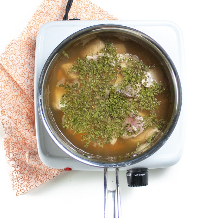 Saucepan full of broth, chicken and parsley.