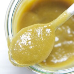 Spoon resting on top of a glass jar filled with mango and kale baby food puree.