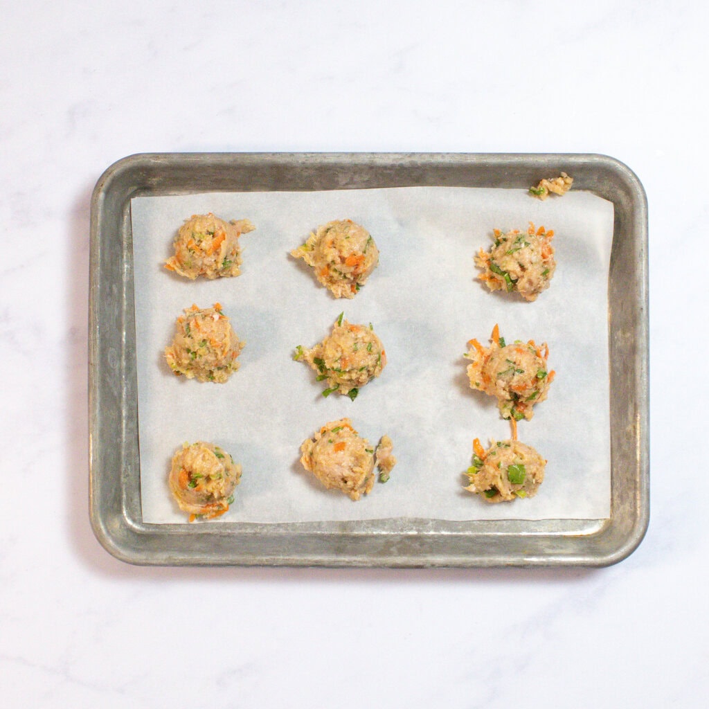 Meatballs on a baking tray ready to get rolled by hand.