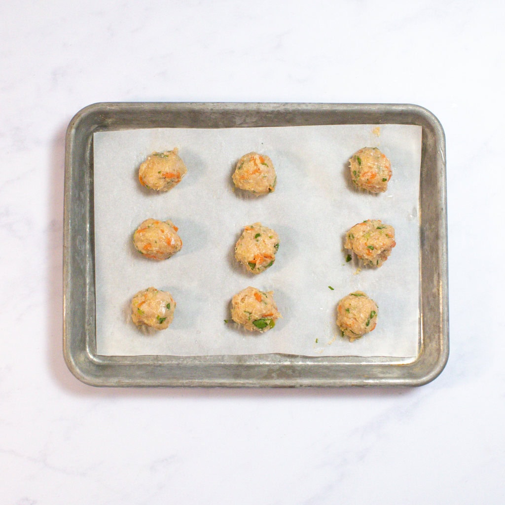Baking sheet with rolled meatballs ready for the oven.