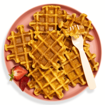 Pink kids plate with a stack of sweet potato waffles with a fork resting on them with a piece of fluffy waffles on it.