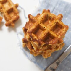 An overhead shot of a stack of sweet potato waffles with one waffle on the white background half eaten - stack of waffles is on a blue napkin