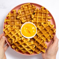 Hand holding pink kids plate full of sweet potato waffles over my white marble kitchen counter.