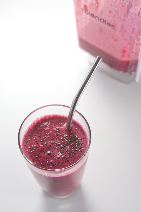 Cherry beet smoothie in a glass with a blender in the background.