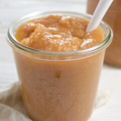 A glass bowl of carrot applesauce with a spoon going inside.
