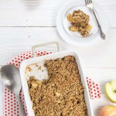 Baked apple crisp is cup with a serving on a plate.