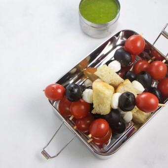 Caprese skewers in a lunch box with a side of basil dipping sauce.