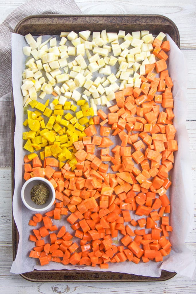 A baking sheet filled with yellow and orange root veggies chopped into small pieces. 