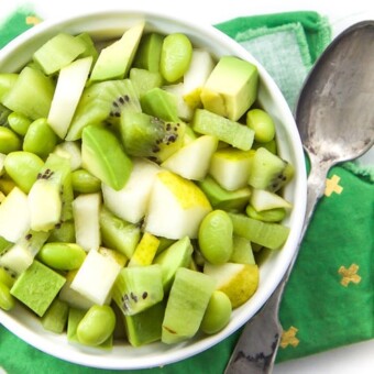 A baby led weaning finger salad in a white bowl with pear, avocado, kiwi, and edamame.