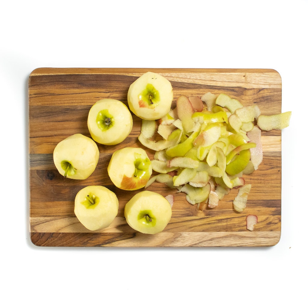 A wooden cutting board with peeled apples away background.