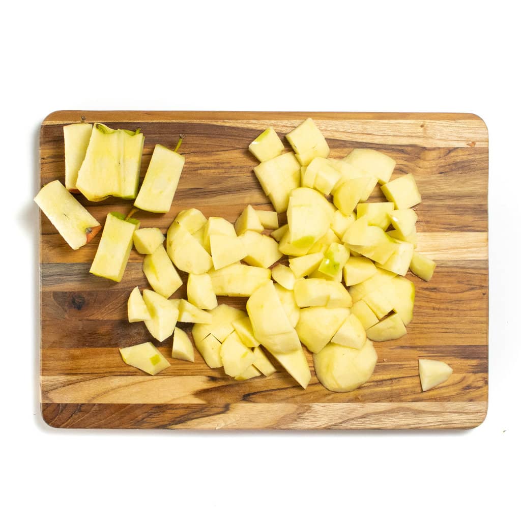 A wooden cutting board with chopped apples on top against a white background.