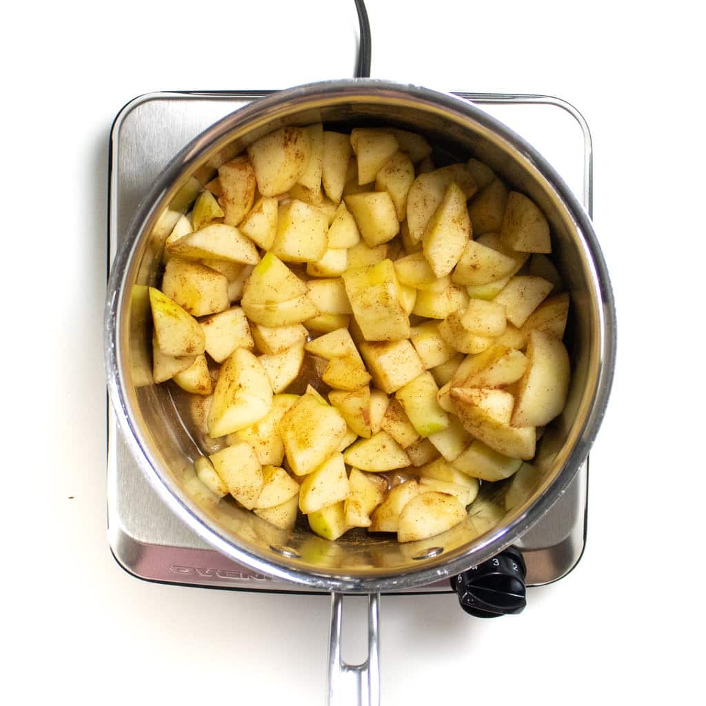 A silver sauce pan with some green apples, cinnamon and vanilla.