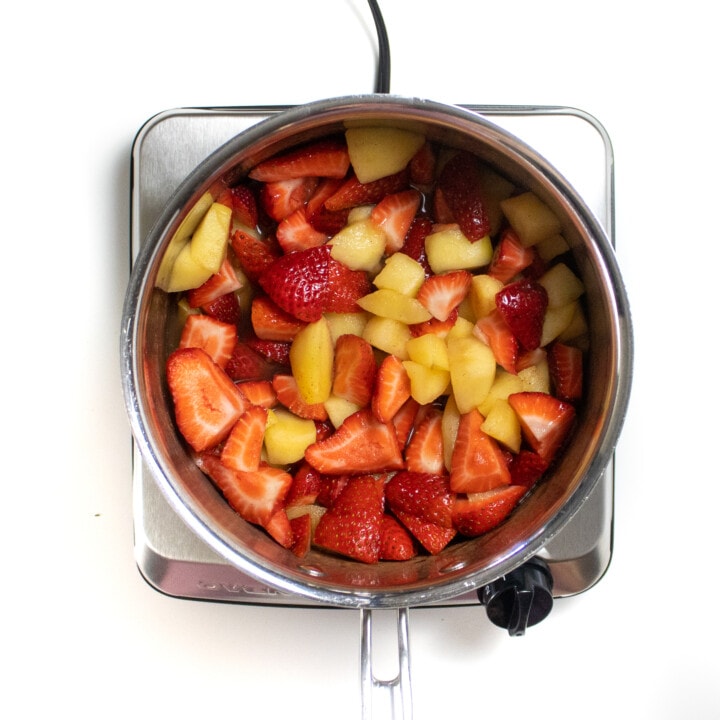 A silver sauce pan with chopped apples and strawberries cooking.