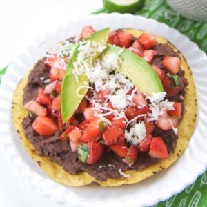 A black bean tostadas topped with strawberry salsa and a avocado on a white plate.