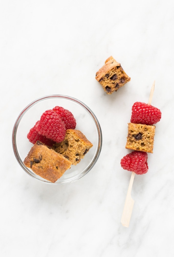 Pumpkin bread and raspberry skewer beside glass dish on marble counter