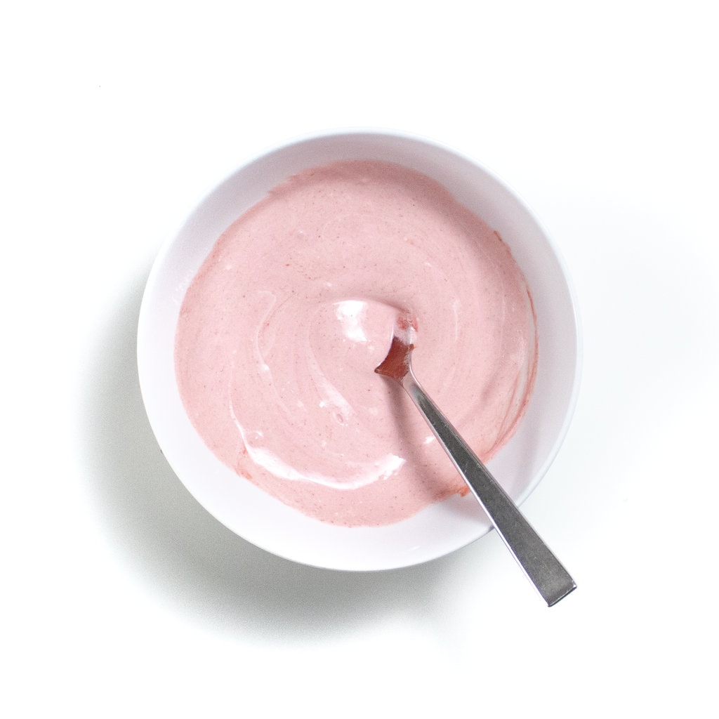 A white bowl against a white background with a mixture of yogurt and a purple baby food puree.