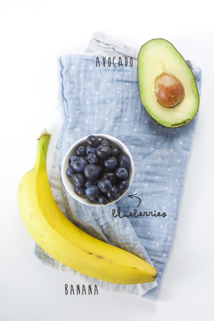 Spread of banana, blueberries and avocado sitting on a blue napkin.