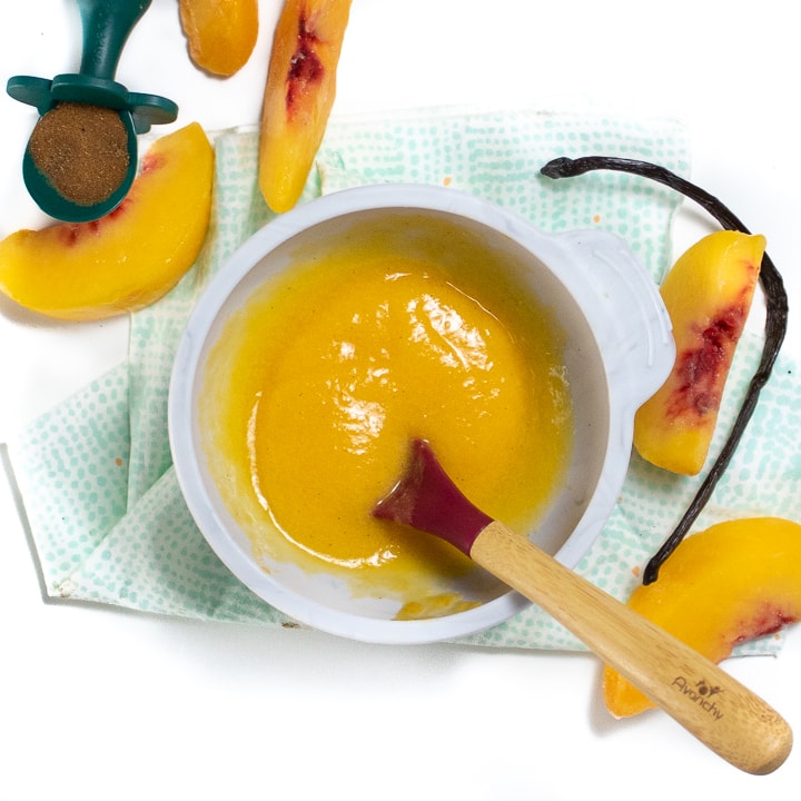 Small gray bowl filled with a peach puree for baby with peaches and vanilla bean besides it.