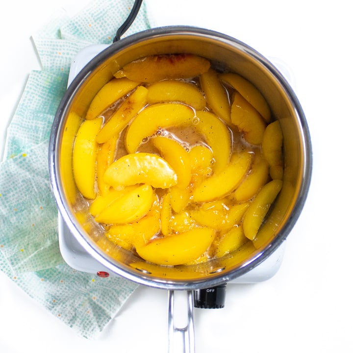 Small silver saucepan full of simmer peaches.