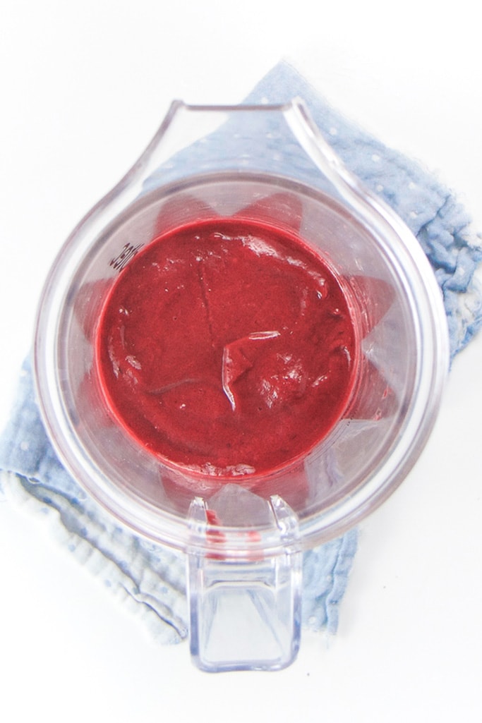 Overhead shot of a clear blender with bright red cherry banana beet baby food puree. 