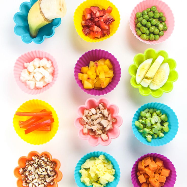 Various finger foods for baby led weaning in colorful silicone baking cups on a white background.