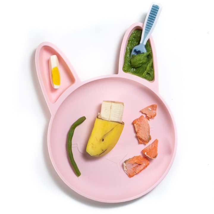 pink baby plate filled with chunks of food and a puree for baby.