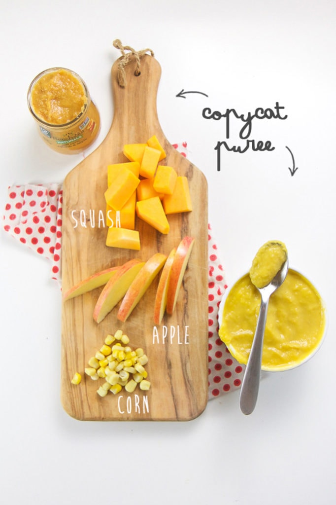 Wood cutting board with chopped apples, corn and squash on top. Sitting next to the cutting board is a bowl full of baby food puree. 