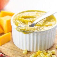 A small white bowl filled with a corn, squash and apple baby food puree.