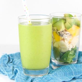 Baby friendly green spinach smoothie in a glass with a separate glass filled with whole smoothie ingredients.