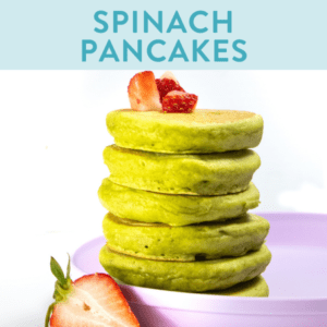 A stack of spinach pancakes against a white background with strawberries on top and on the side.