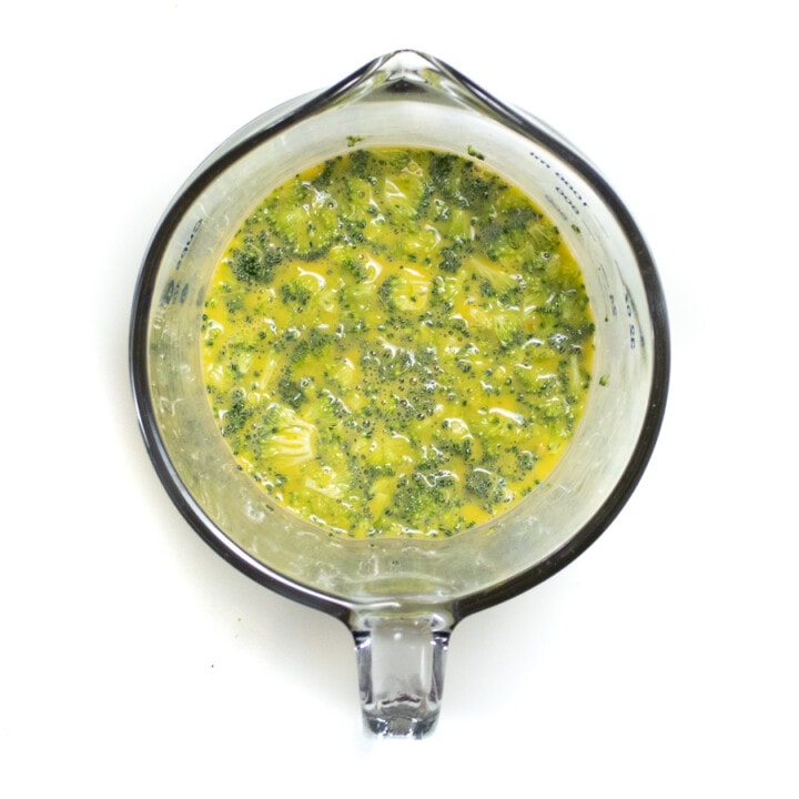 Big measuring cup filled with eggs, broccoli and cheese, all mixed together.