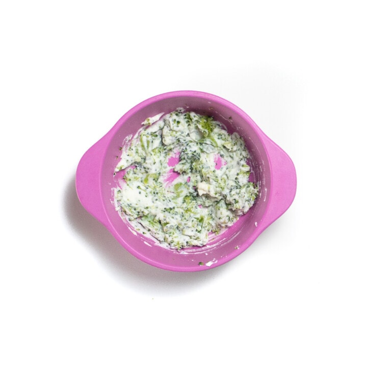 Pink baby bowl with steamed broccoli and ricotta mixed together.